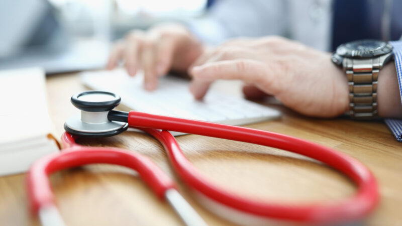 Doctor is typing on keyboard next to stethoscope. Medical care and health concept